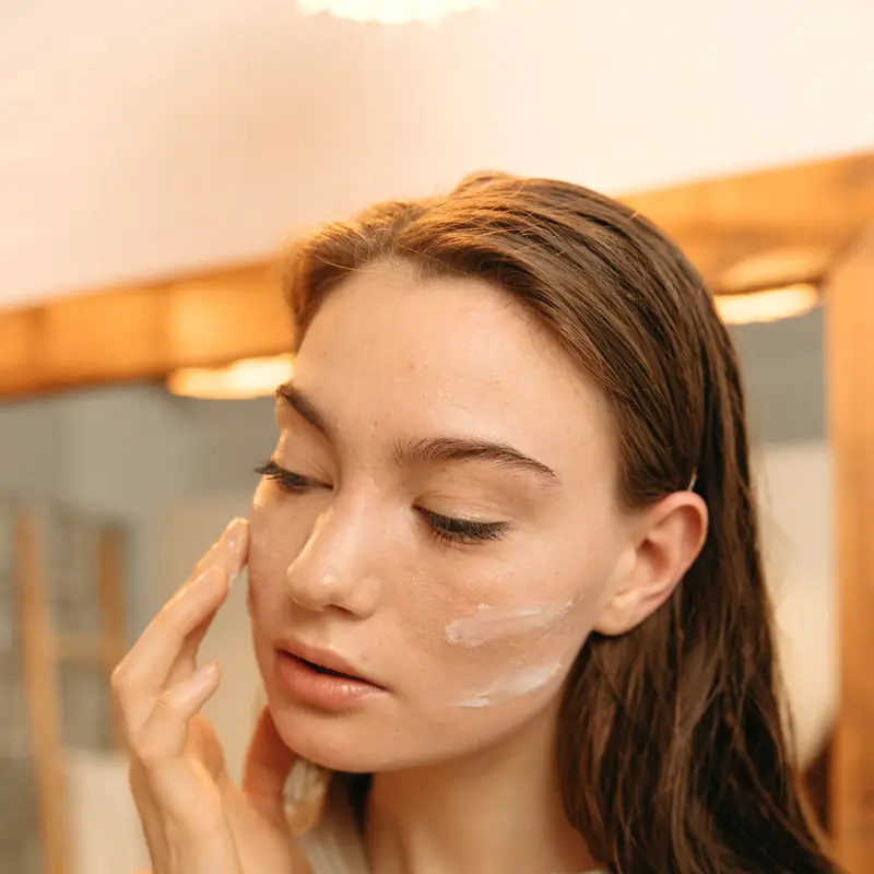 Después: mujer joven extendiendo crema por la cara frente a un espejo
