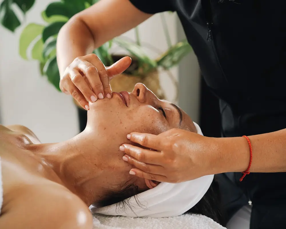 Esteticista haciendo un masaje facial a una clienta tumbada en la camilla